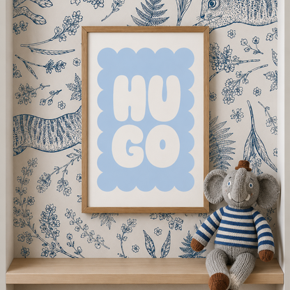 A framed nursery art print with the word 'HUGO' in white letters on a light blue background, styled on a wooden shelf against blue-and-beige illustrated wallpaper with a stuffed elephant toy.