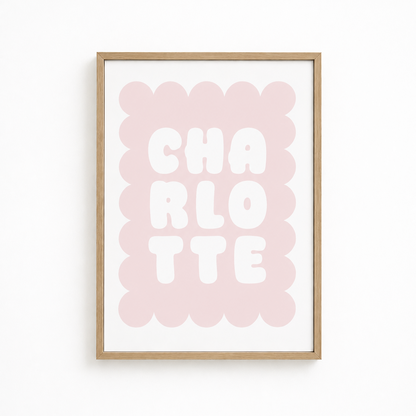 A framed typographic wall art print featuring the word 'CHARLOTTE' in large white letters over a soft pink scalloped rectangle, mounted in a light natural wood frame against a white wall.